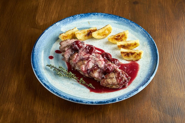 Delicious baked confit duck breast with berry sauce and potatoes, served on a blue plate