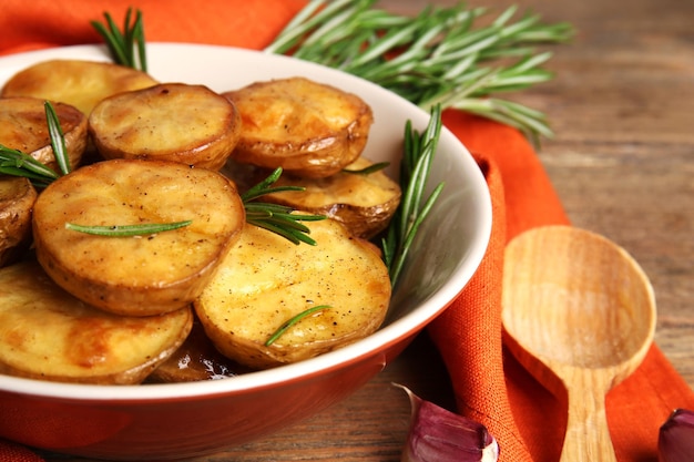 Delicious baked potato with rosemary in bowl on table close up