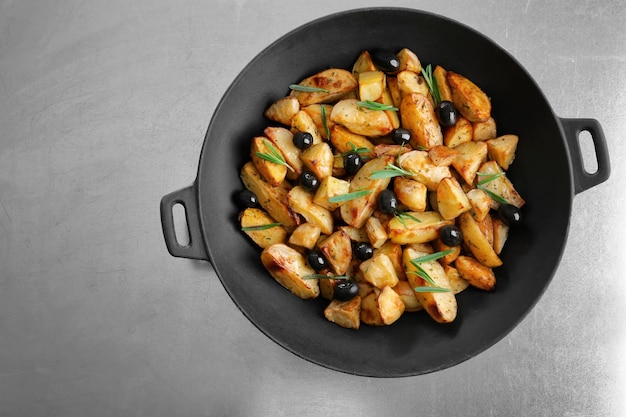 Delicious baked potatoes with rosemary and olives in pan on table