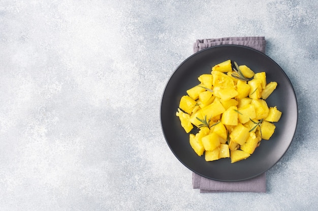 Delicious baked potatoes with spices cheese and rosemary on a black ceramic plate, a gray concrete background, copy space.