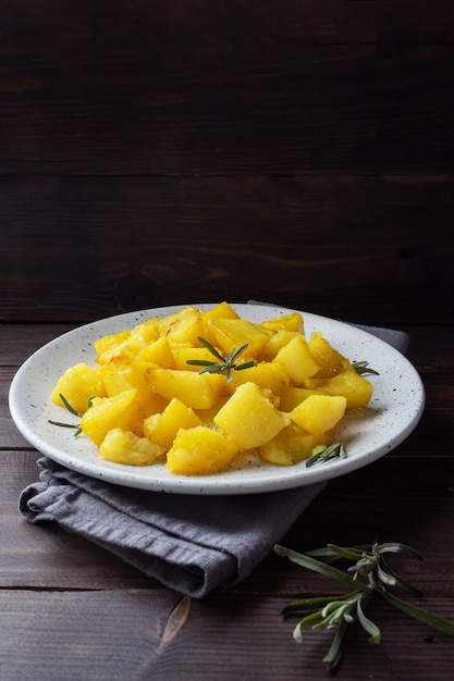 Delicious baked potatoes with spices cheese and rosemary on a plate, a dark wooden table. Copy space