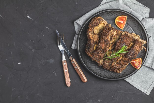 Photo delicious baked roast pork meat in black ceramic plate with garlic and spices dish for dinner top view flat lay dark concrete surface copy space for you text