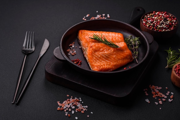 Delicious baked salmon red fish steak with spices and herbs on a dark concrete background