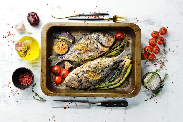 Delicious baked whole fish with herbs and lemon in a metal baking tray Dorado On a white wooden background