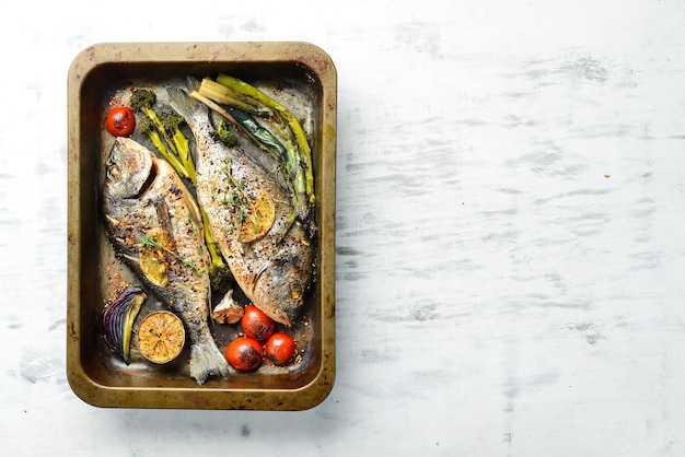 Delicious baked whole fish with herbs and lemon in a metal baking tray Dorado On a white wooden background