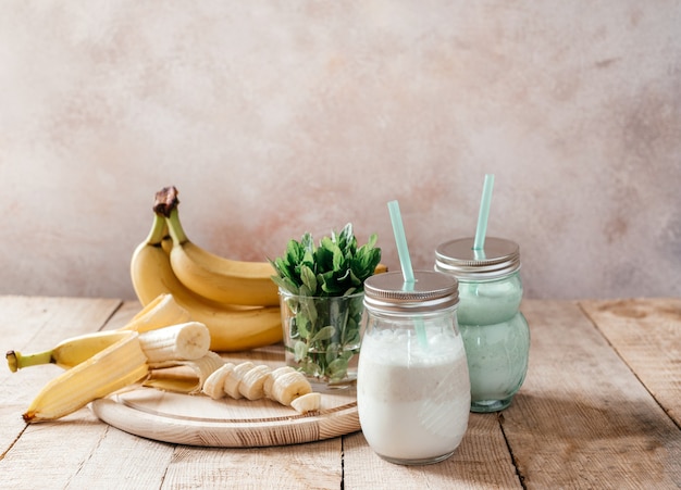 Delicious banana yogurt smoothie in a latte coffee glass with handle with mint leaves and bananas with handle on wooden background