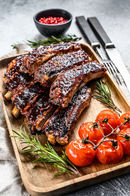 Delicious barbecued ribs seasoned with a spicy basting sauce and served with baked tomatoes. Gray background. Top view