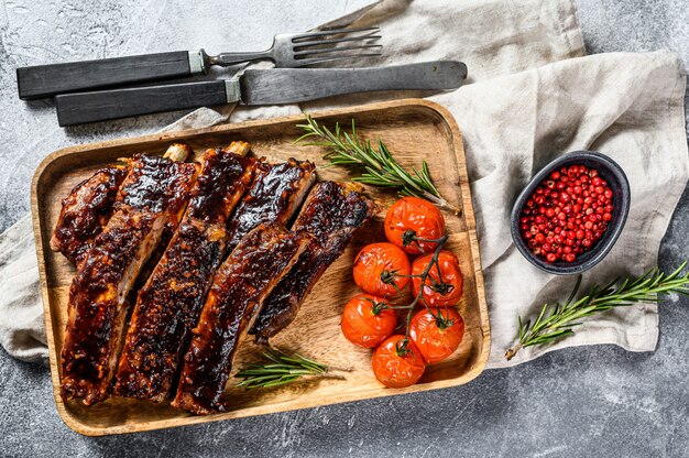 Delicious barbecued ribs seasoned with a spicy basting sauce and served with baked tomatoes. Gray background. Top view