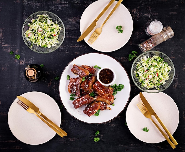 Delicious barbecued spare ribs on plate on dark background Tasty bbq meat Top view flat lay