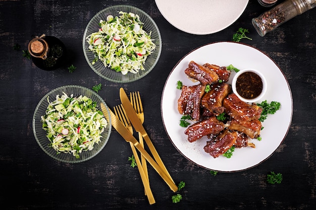 Delicious barbecued spare ribs on plate on dark background Tasty bbq meat Top view flat lay