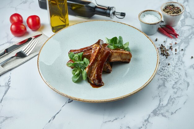 Delicious BBQ pork ribs in sauce in a blue plate on a marble surface