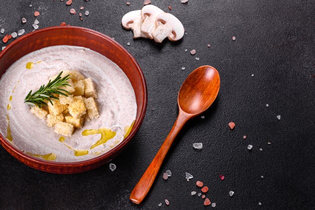 Delicious beautiful mushroom soup in a brown plate with a wooden spoon on a dark brown background