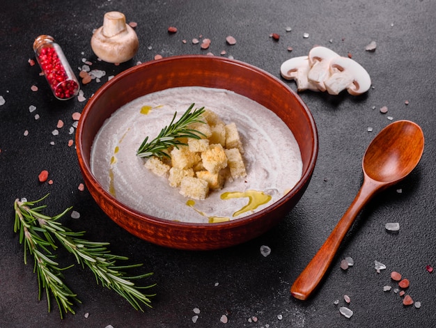 Delicious beautiful mushroom soup in a brown plate with a wooden spoon on a dark brown surface