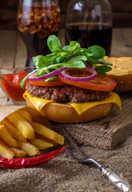 Delicious beef burger with chips and soda on wooden table.