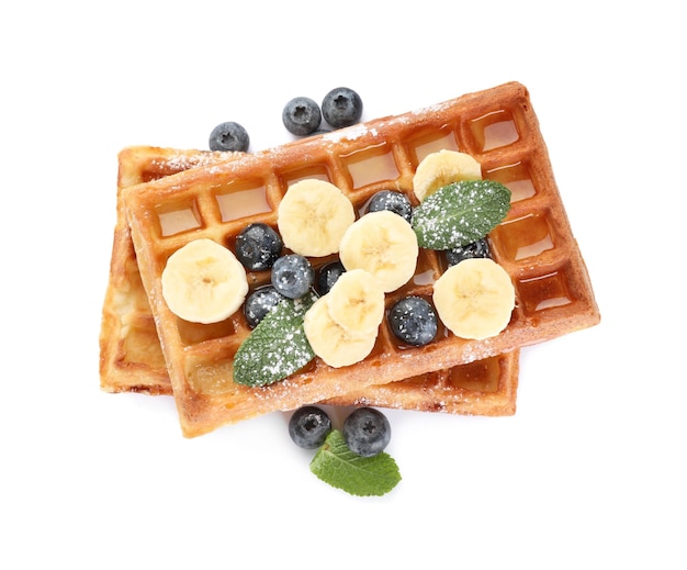 Delicious Belgian waffles with blueberries and banana on white background top view