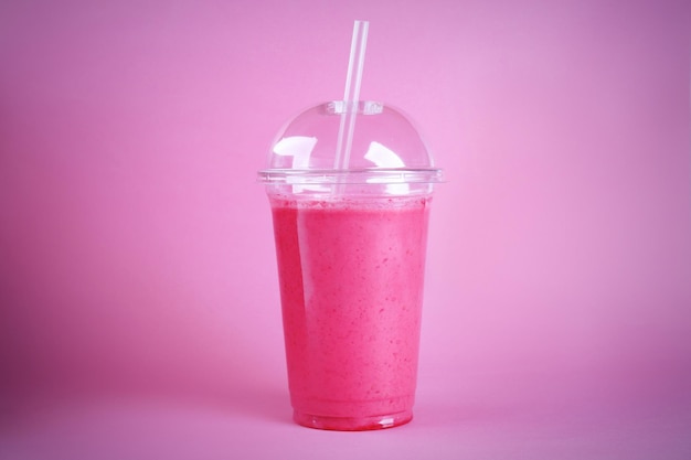 Delicious berry milkshake in plastic cup on pink background