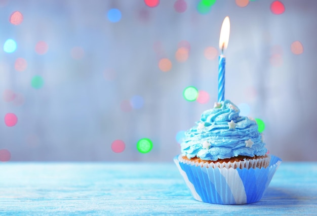 Delicious birthday cupcake on table on light background