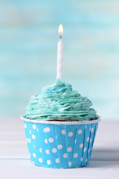 Delicious birthday cupcake on table on light blue background