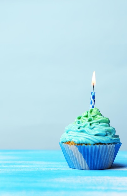 delicious birthday cupcake on table on light blue background