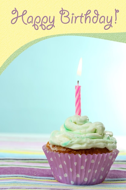 Delicious birthday cupcake on table on light blue background