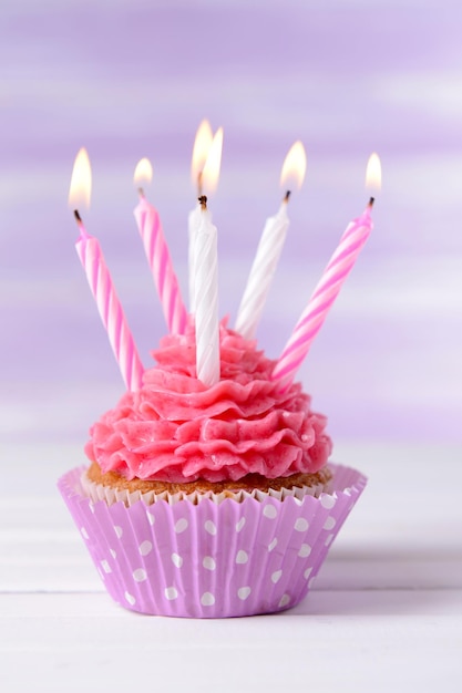 Delicious birthday cupcake on table on light purple background