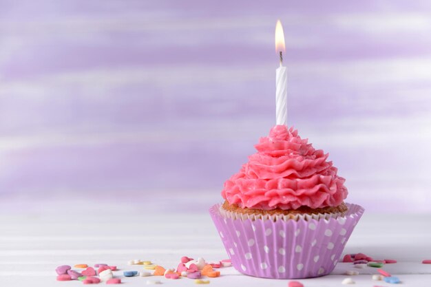 delicious birthday cupcake on table on light purple background