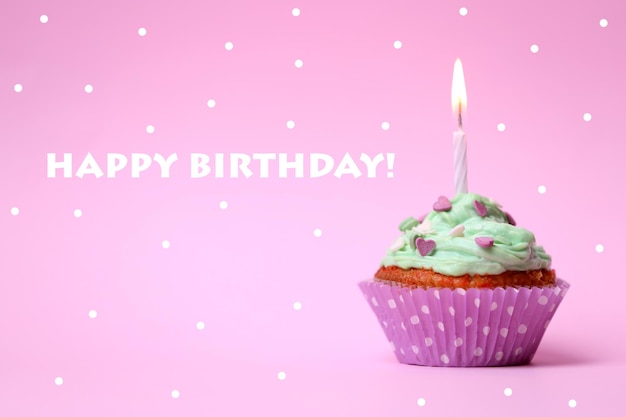 Delicious birthday cupcake on table on pink background