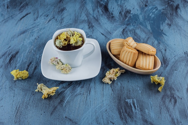 Delicious biscuits with cup of herbal tea on blue surface. 