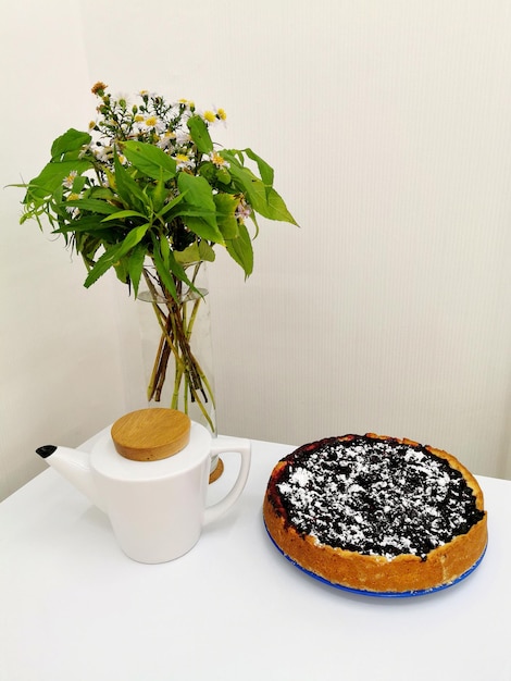 Вкусный пирог с черникой и шапочкой, букет цветов и белый чайник с чаем