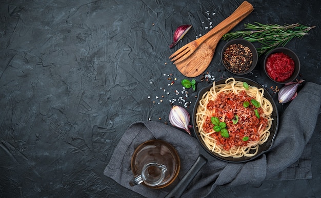 黒の背景にフライパンでパルメザンチーズとスパイスのおいしいボロネーゼパスタ。