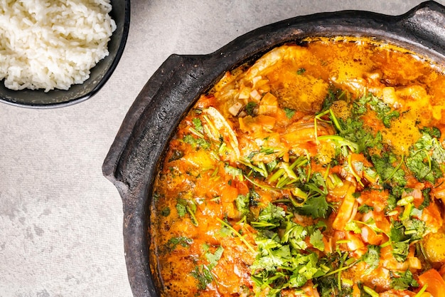 Delicious Brazilian fish moqueca with tomato onion olive oil coriander and orocum seed Made in clay pot on white table and black background