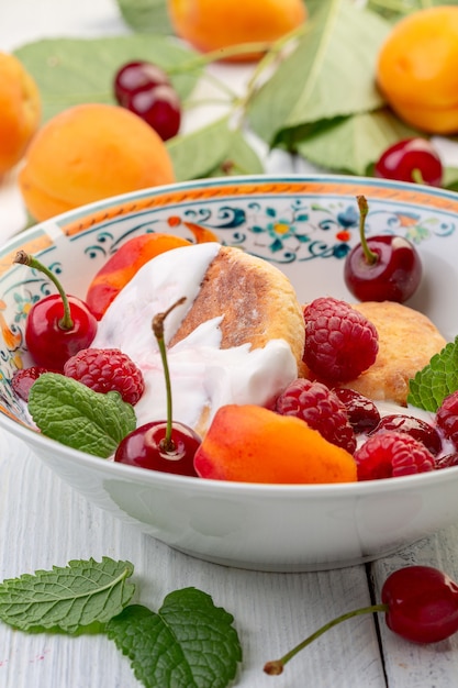 Delicious breakfast - cottage cheese fritters, cottage cheese pancakes with raspberries, cherries, apricots and cream sauce in a white plate, selective focus.