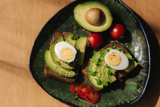 Photo delicious breakfast at home. sandwich with fresh sliced avocado above rye bread with cherry tomatoes