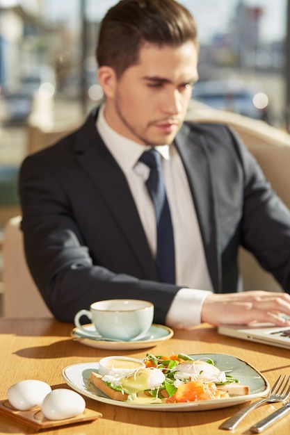 Delicious breakfast on the plate, handsome business man working on laptop on the background