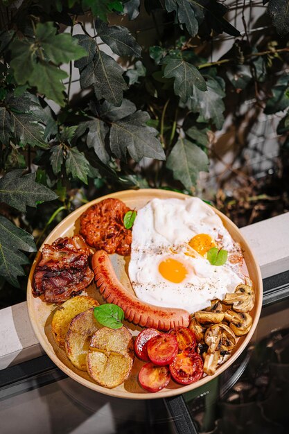 卵ベーコンソーセージ野菜を備えた美味しい朝食皿が茂った緑のなかで屋外で提供されています