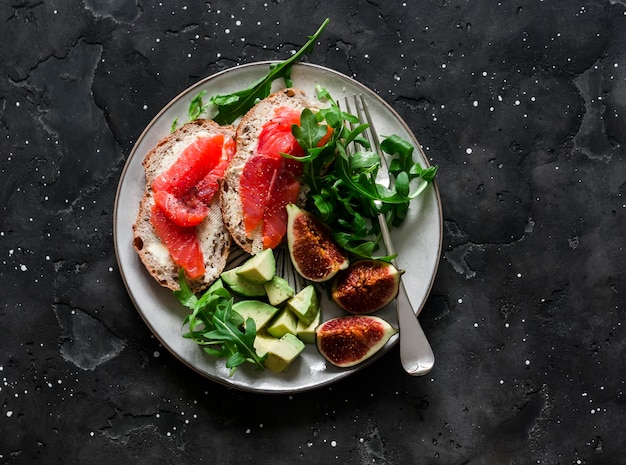 Photo delicious breakfast snack appetizer salmon sandwich avocado arugula figs on a dark background top view