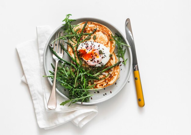 Delicious breakfast snack cheese pancakes with poached egg asparagus and arugula on a light background top view