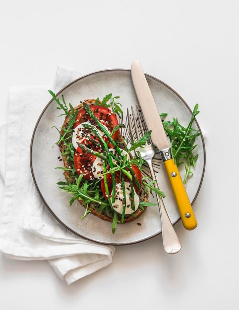 Delicious breakfast snack whole grain bread sandwich with tomato mozzarella arugula and asparagus on a light background top view