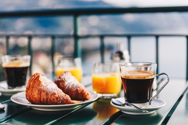 イタリアの海の景色を望むバルコニーで提供されるコーヒーペストリーとオレンジジュースのおいしい朝食