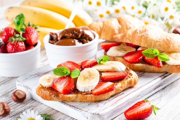 Вкусный завтрак со свежими круассанами, шоколадом, бананом и клубникой на деревянном столе