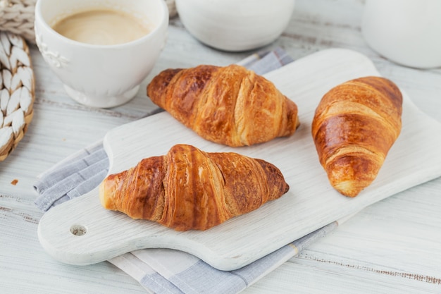 Delicious breakfast with fresh croissants and cup of coffee on a white wooden. Delicious Baking