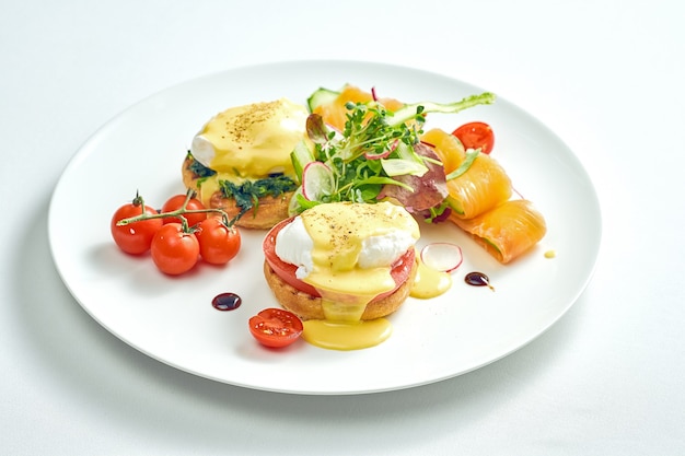 데친 달걀 토스트와 hollandaise 소스, 흰색 접시에 살짝 소금에 절인 연어로 맛있는 아침 식사. 흰색 표면에 격리.