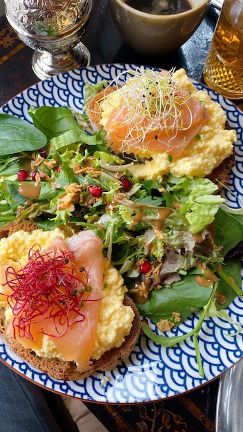 Piatto delizioso per il brunch toast con salmone affumicato, uova strapazzate, germogli e insalata