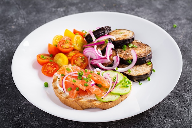 Delicious brunch  salmon  bread cream cheese sandwiches and arugula, tomatoes salad on a dark background.