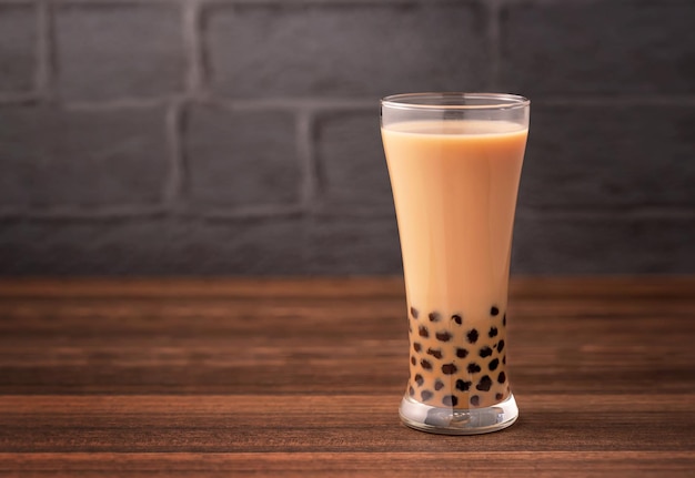 Delicious bubble milk tea with tapioca pearl ball in glass on wooden table and dark gray brick background popular food and drink in Taiwan close up