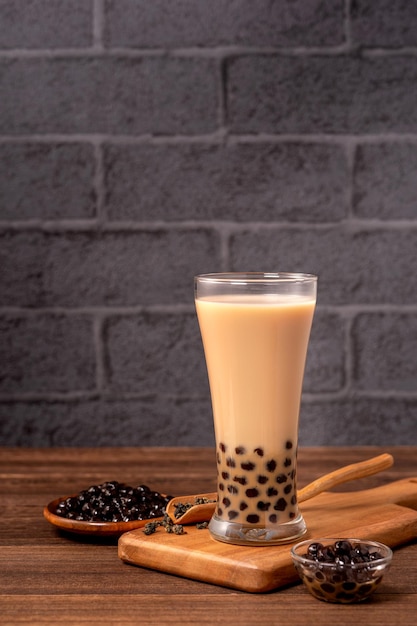 Delicious bubble milk tea with tapioca pearl ball in glass on wooden table and dark gray brick background popular food and drink in Taiwan close up