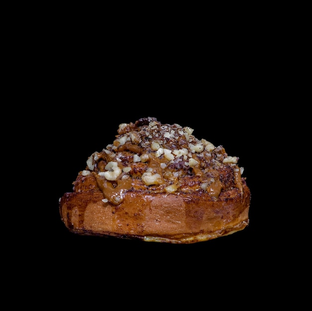 Delicious bun with cream and nuts on a black background