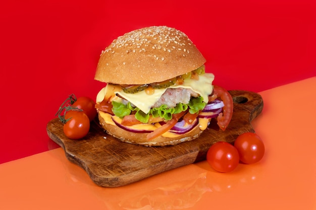 Delicious burger on the board with cutlet tomatoes and cheese cucumber and lettuce On a red background Fast food