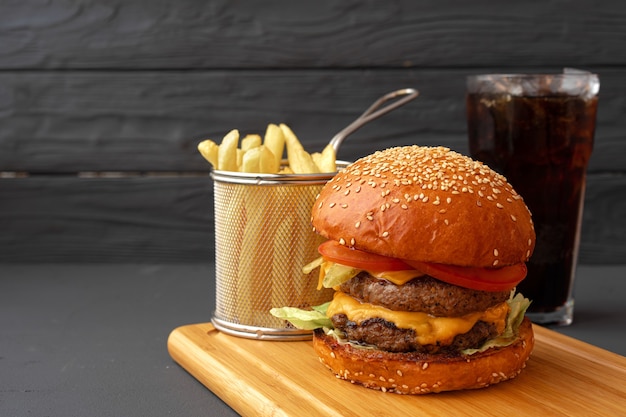 Delicious burger and fries on wooden board against black background, front view