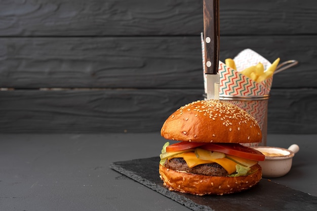 Delicious burger and fries on wooden board against black background